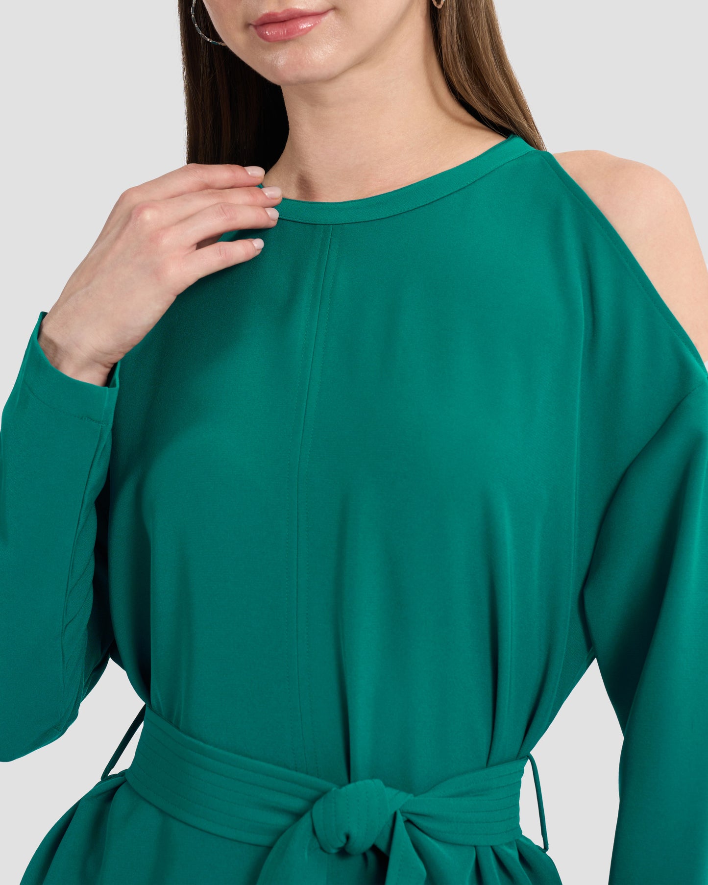A woman wearing a teal monogram-embroidered cold-shoulder top with a waist sash and a gunmetal GFF embellishment on the hem paired with coordinated trousers.