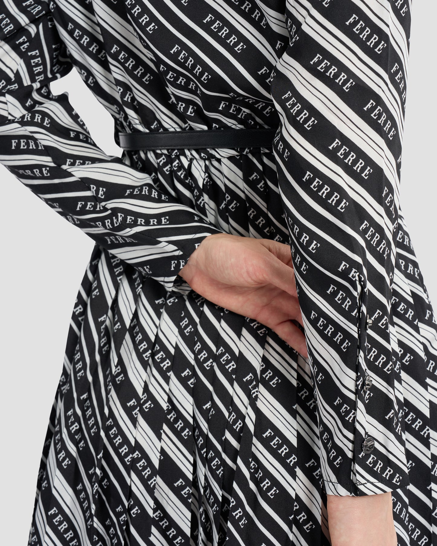 A woman wearing a black and white striped, long-sleeve shirt dress with a collared neckline and pleated skirt. The dress is cinched at the waist with a matching belt, styled with black open-toe heels for a sophisticated look.