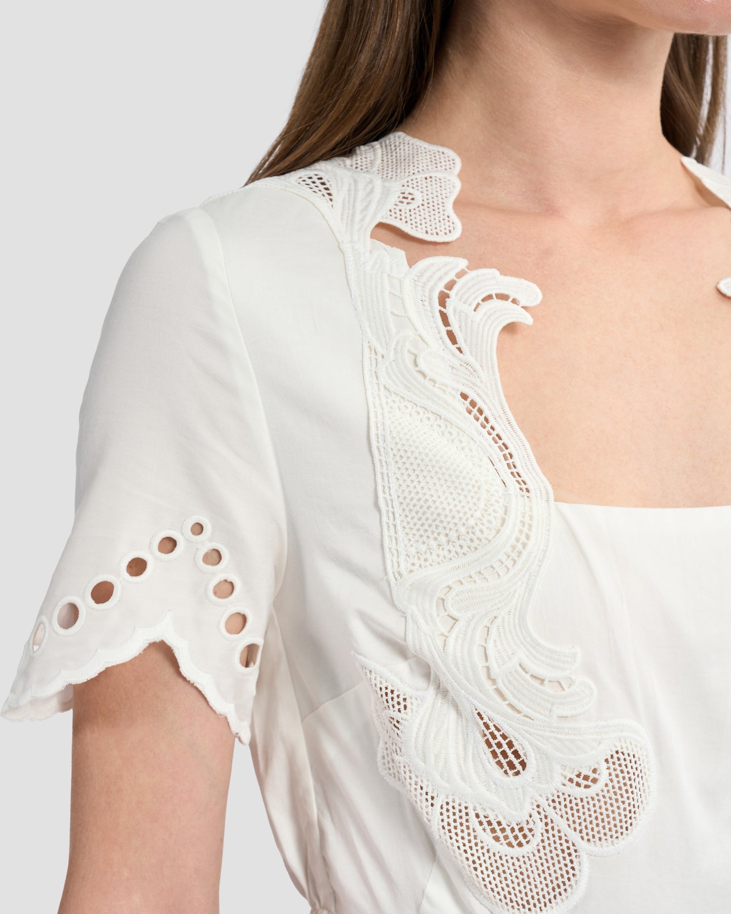 A woman wearing a white midi dress with intricate cutout embroidery details on the bodice and sleeves.