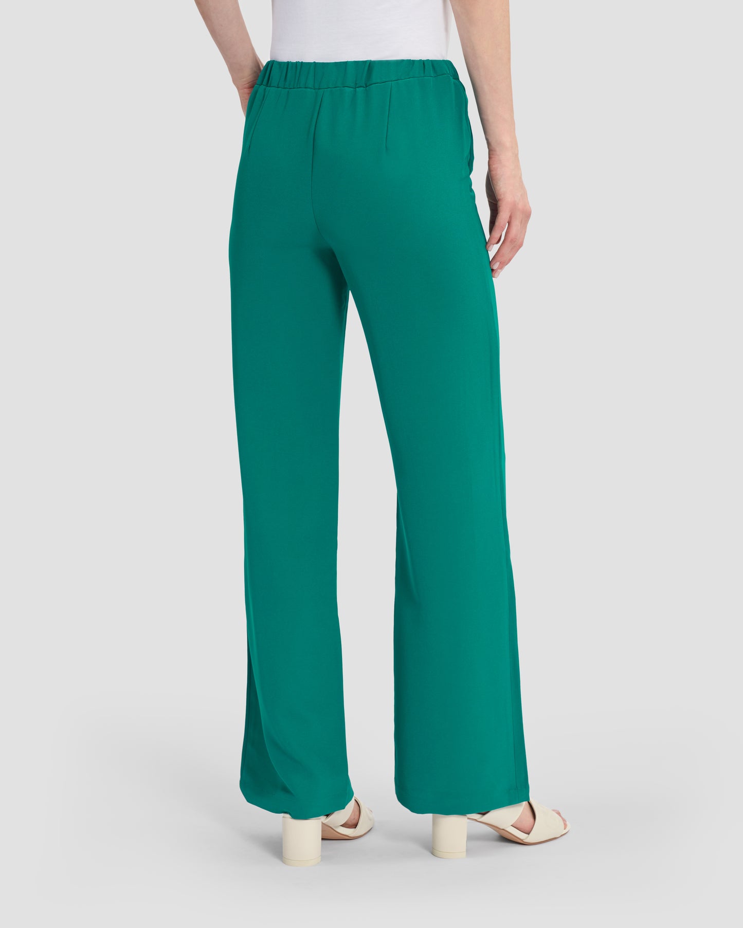 Woman wearing teal flared trousers embellished with a gunmetal monogram at the waistband, paired with beige sandals.