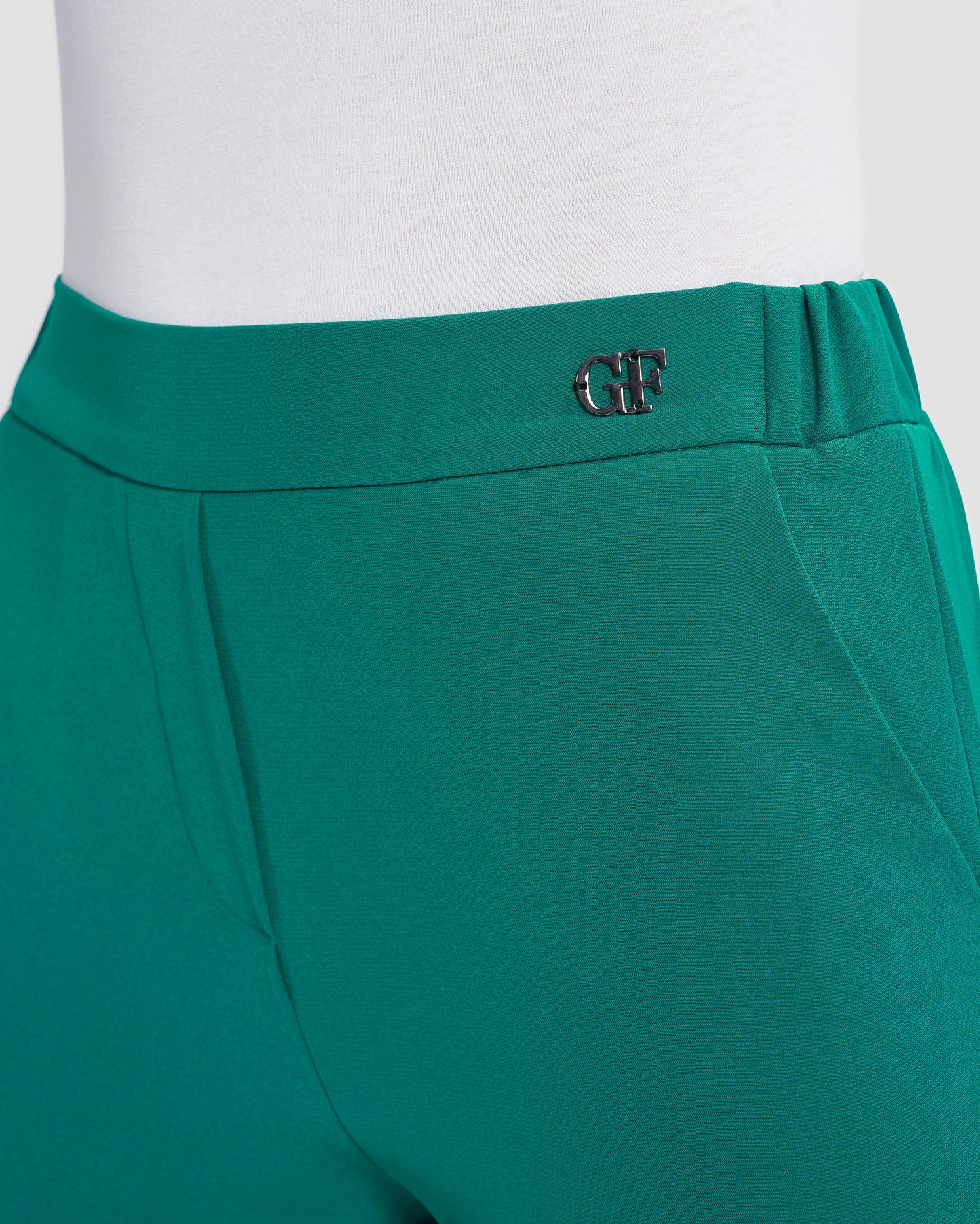 Close-up look of teal flared trousers embellished with a gunmetal monogram.