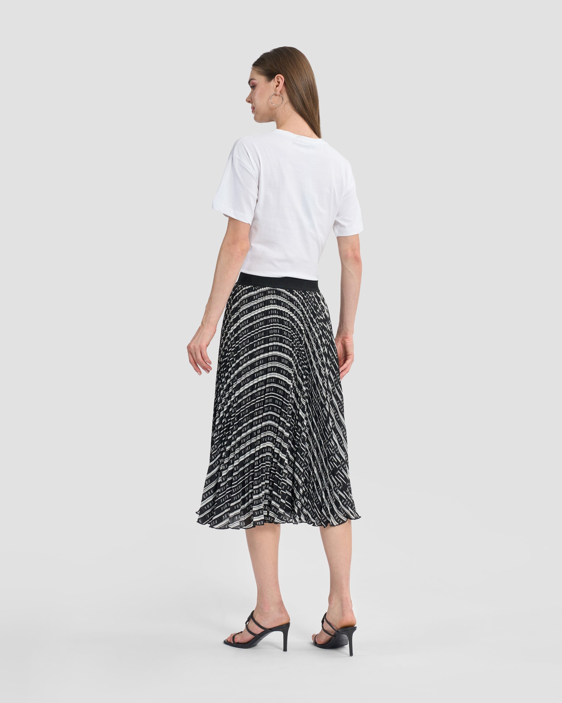 Woman wearing a Gianfranco Ferré black and white pleated midi skirt, paired with black high-heeled sandals